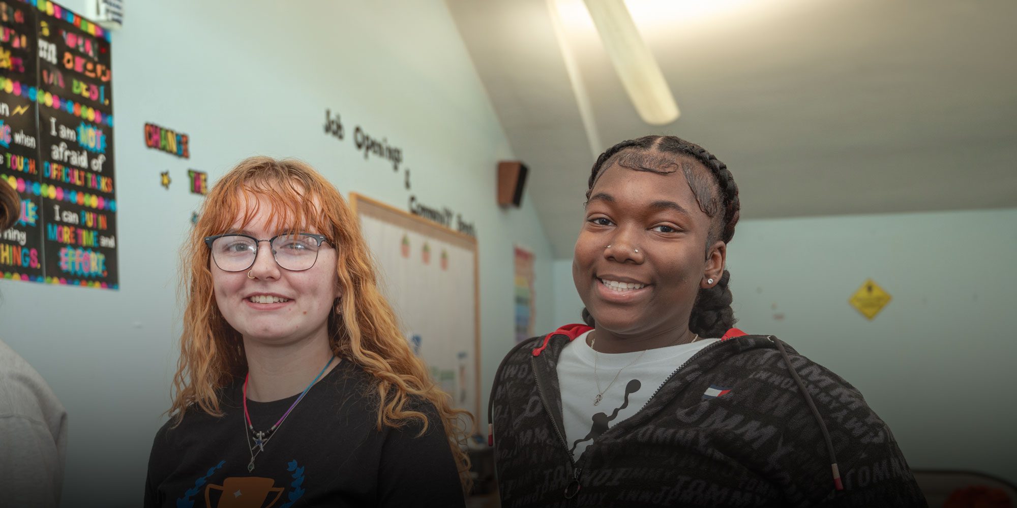 Two smiling students standing together in a classroom.